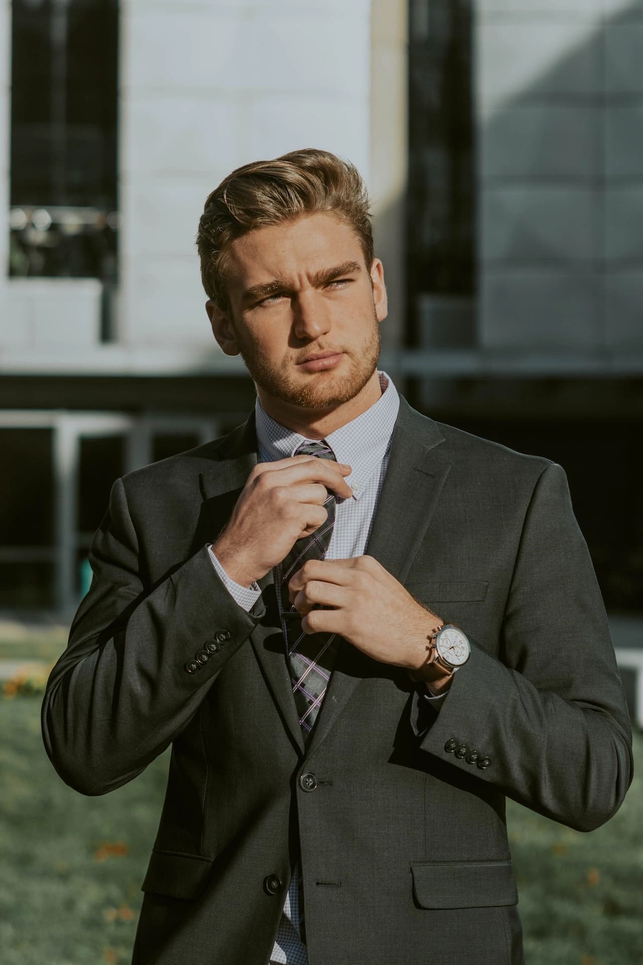 Man in a suit adjusting his tie outside an office building